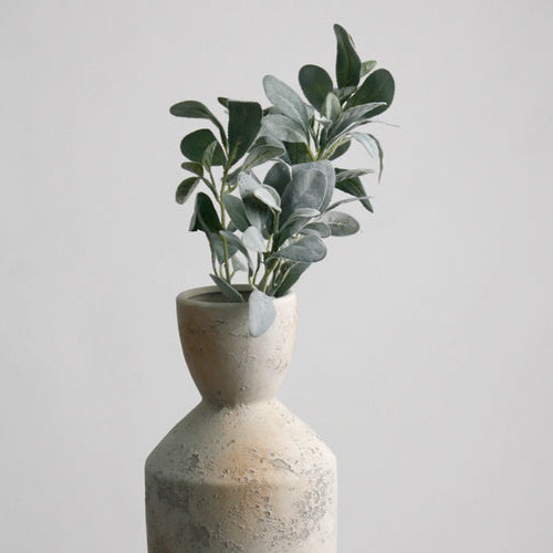 Decorative vase with a plant on a white surface and light gray background