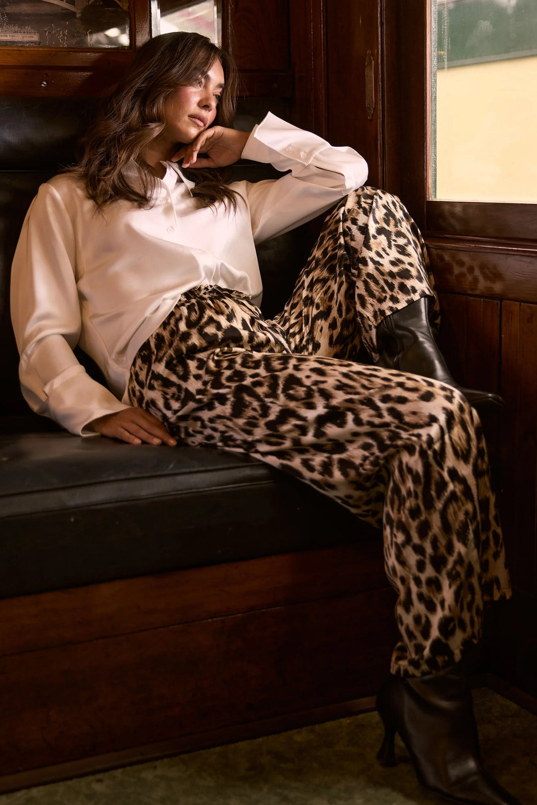 Woman sitting on a train bench wearing a white blouse and leopard print pants.