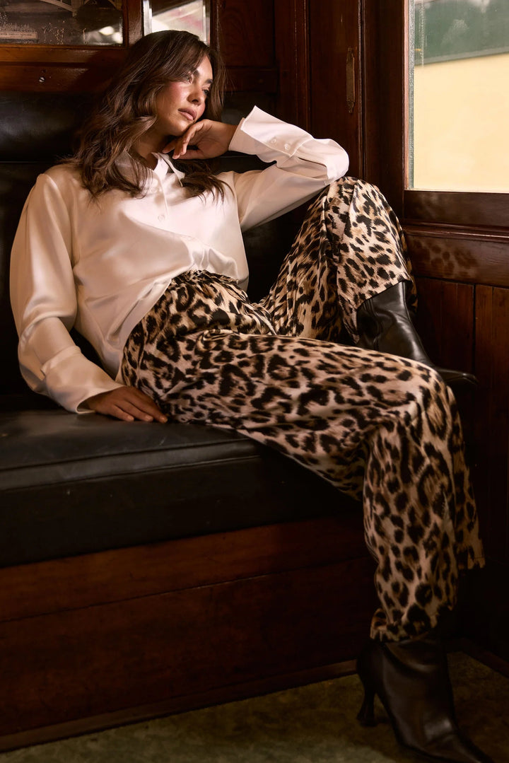 Woman sitting on a train bench wearing a white blouse and leopard print pants.