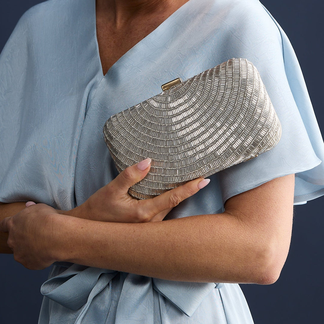 Woman in a light blue dress holding a silver clutch against a dark background