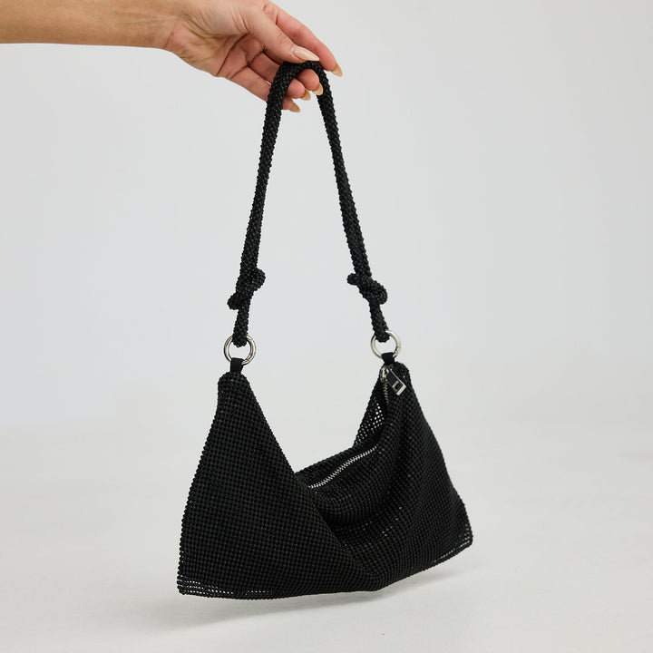 Black textured handbag held by a hand against a light gray background