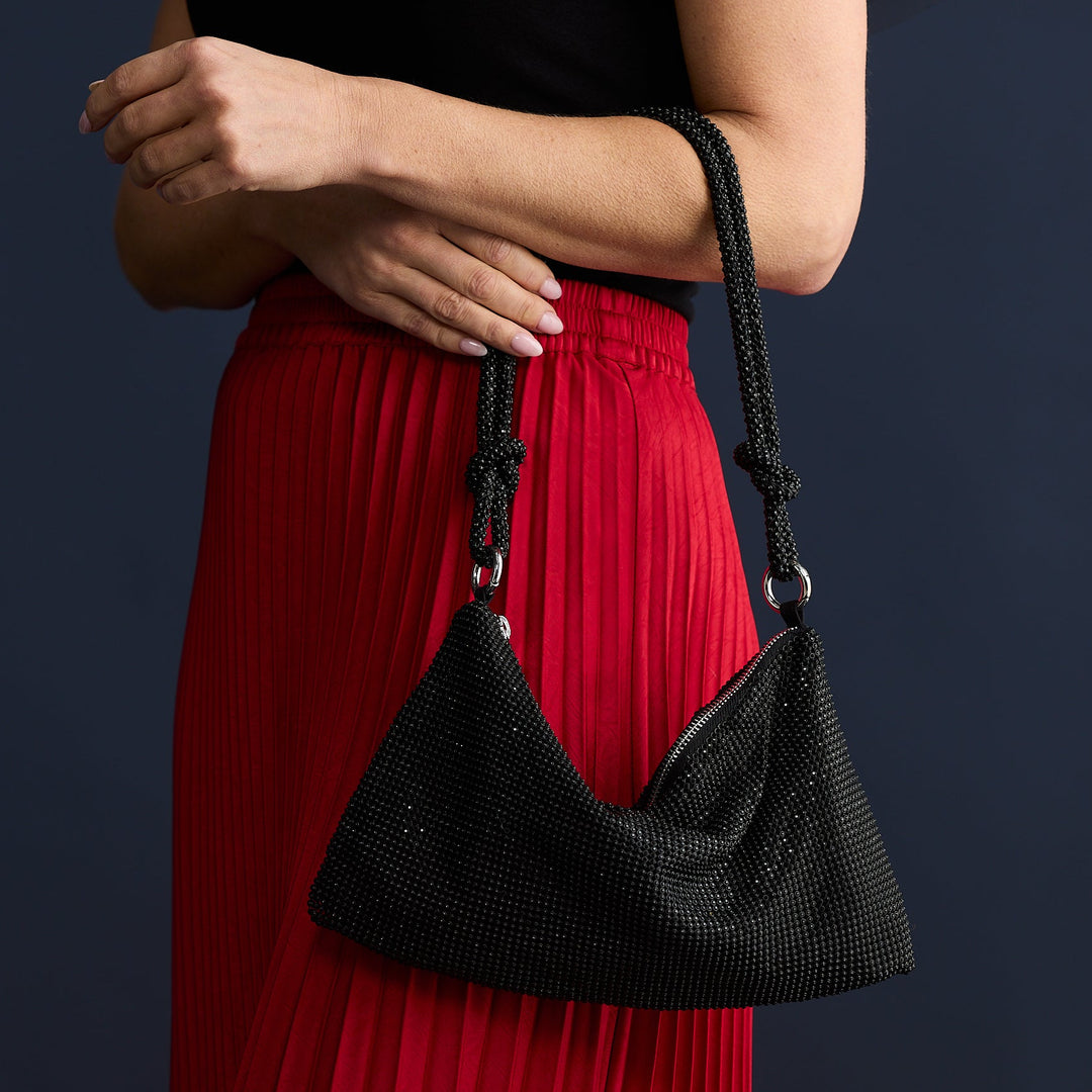Person wearing a black top and red skirt holding a black handbag against a dark background