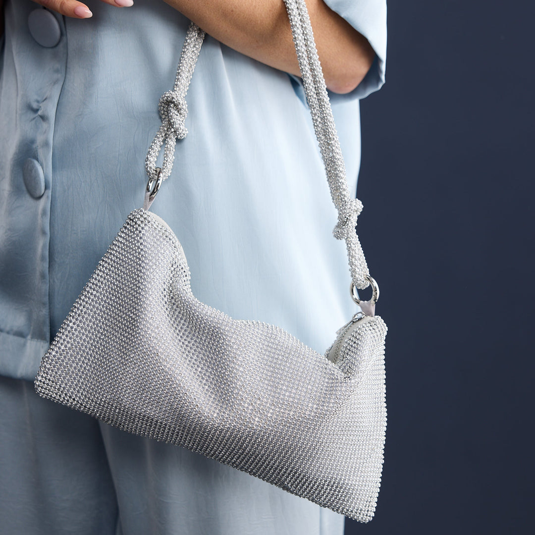 Person holding a textured gray handbag against a dark background