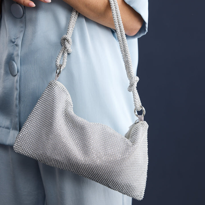 Person holding a textured gray handbag against a dark background