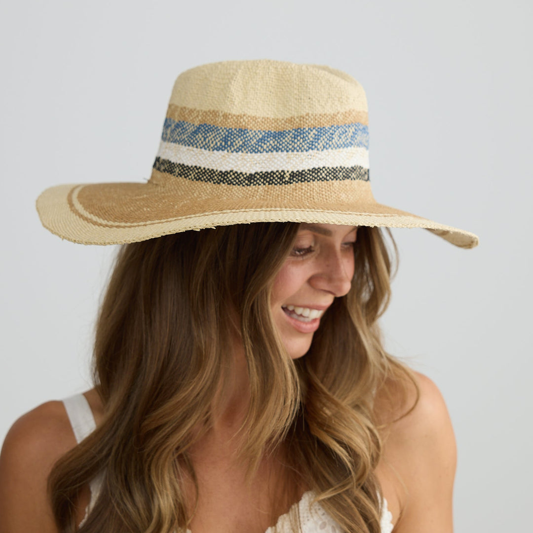 Woman wearing a wide-brimmed hat with a blue band against a plain background