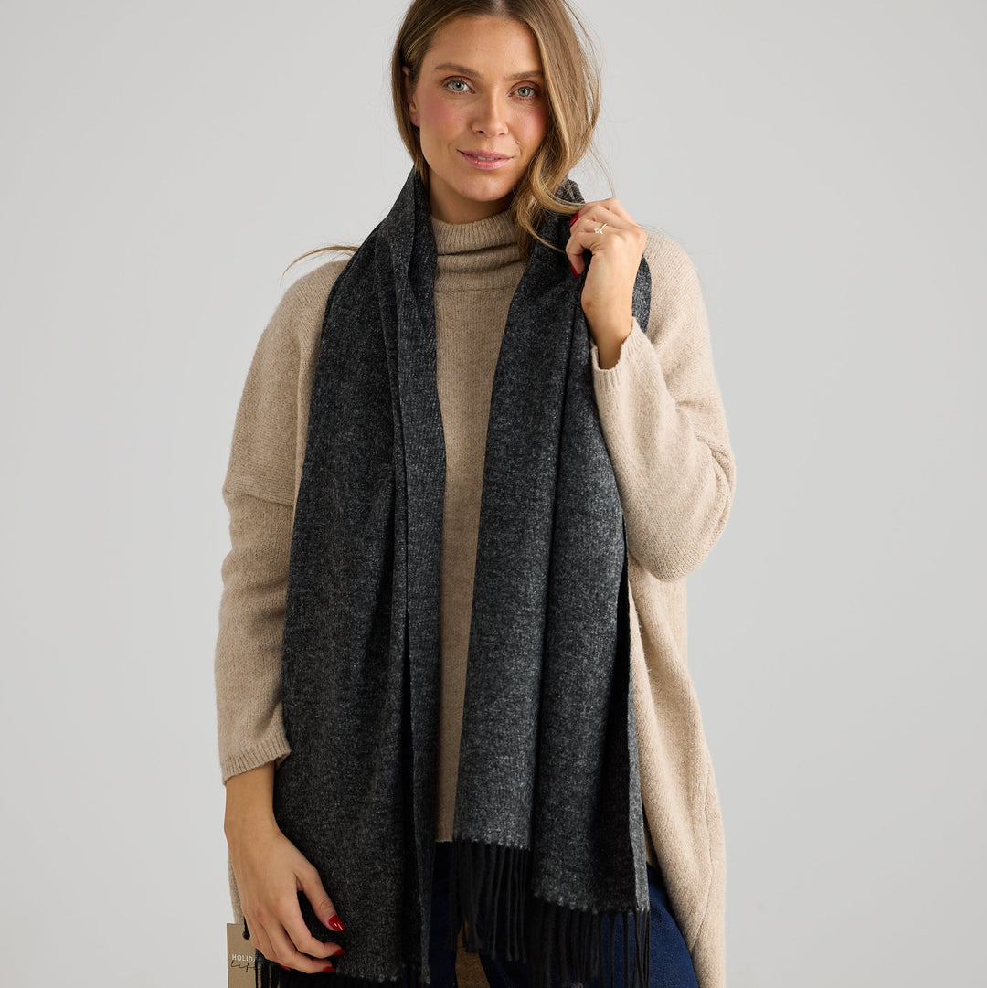 Woman wearing a beige coat and dark gray scarf on a plain background