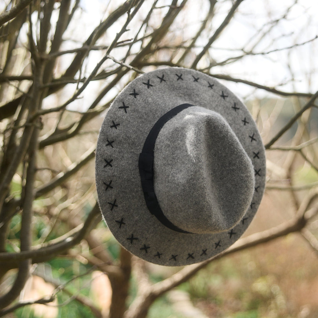 Gray fedora hat hanging on a tree branch with a blurred natural background
