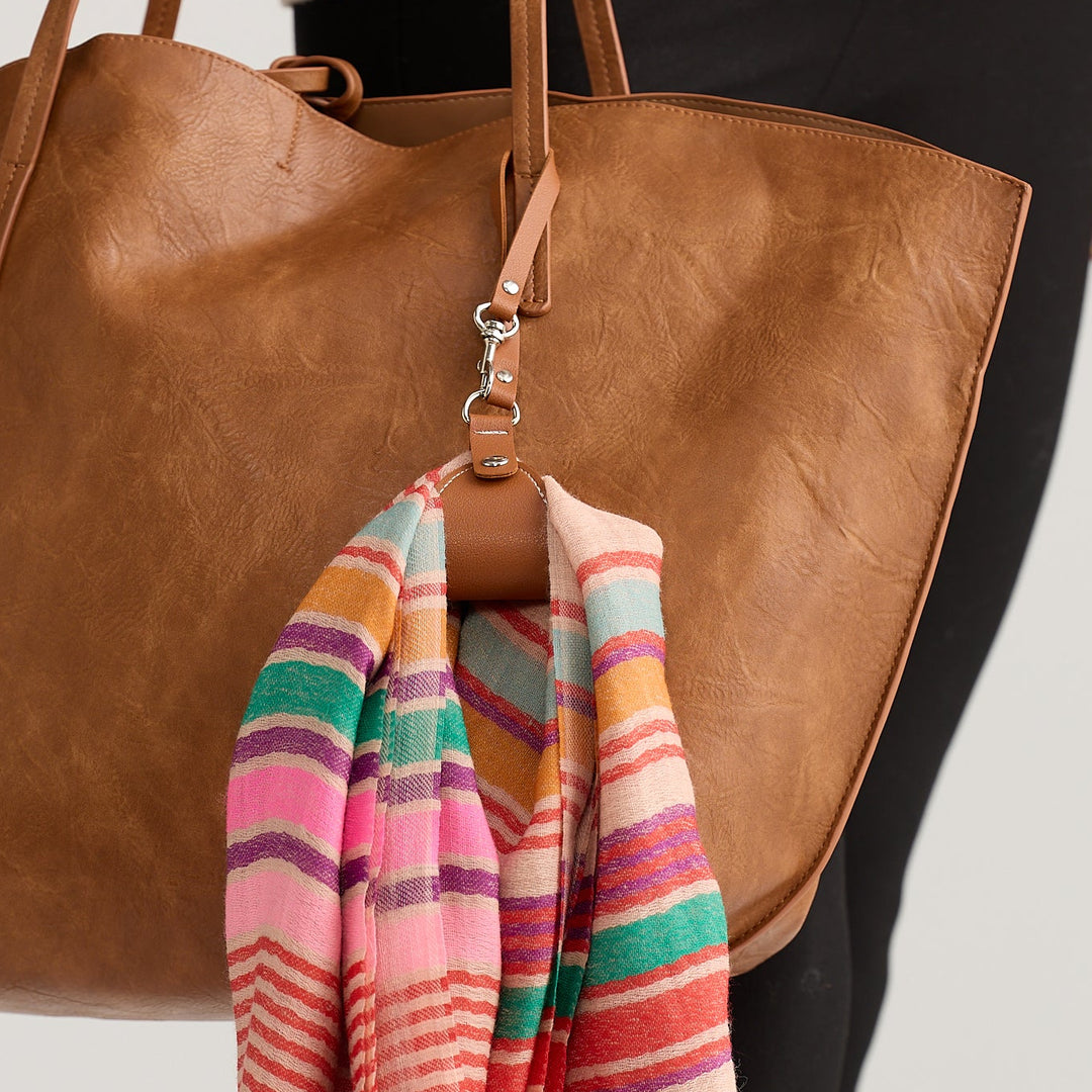 Brown leather tote bag with a colorful striped scarf draped over it on a neutral background