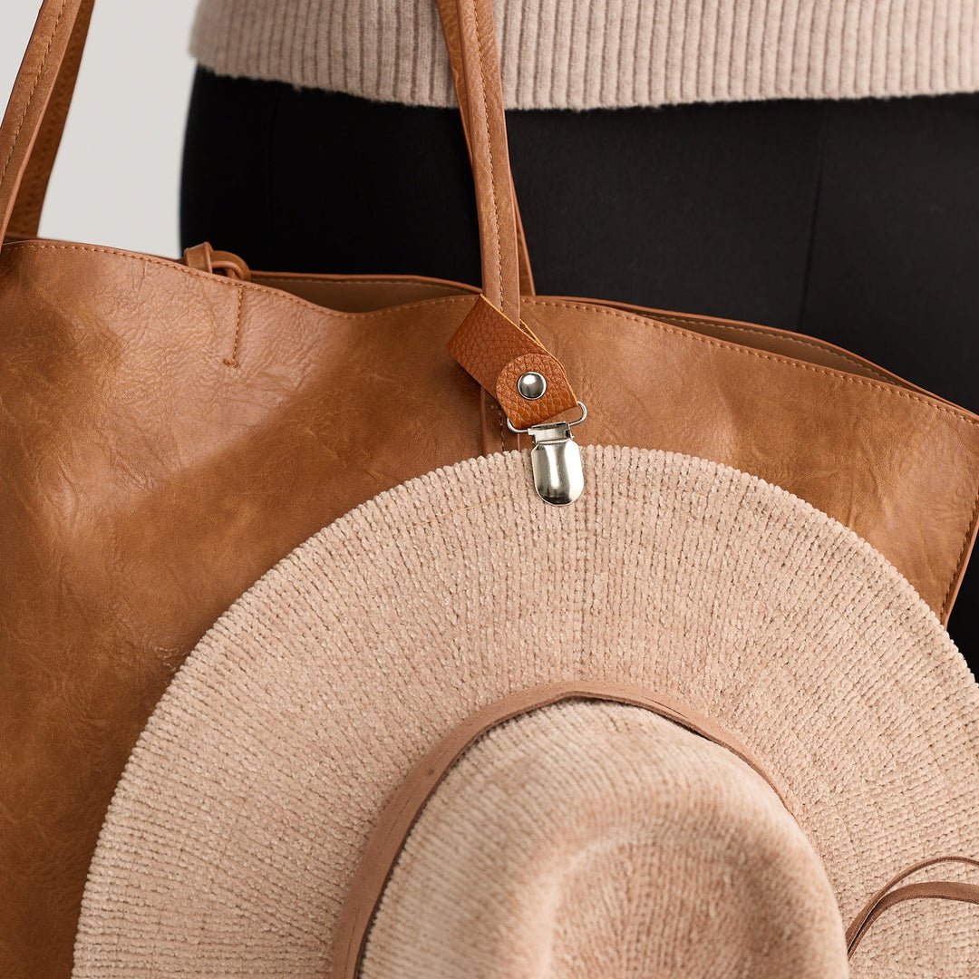 Brown leather tote bag with a beige hat on a neutral background