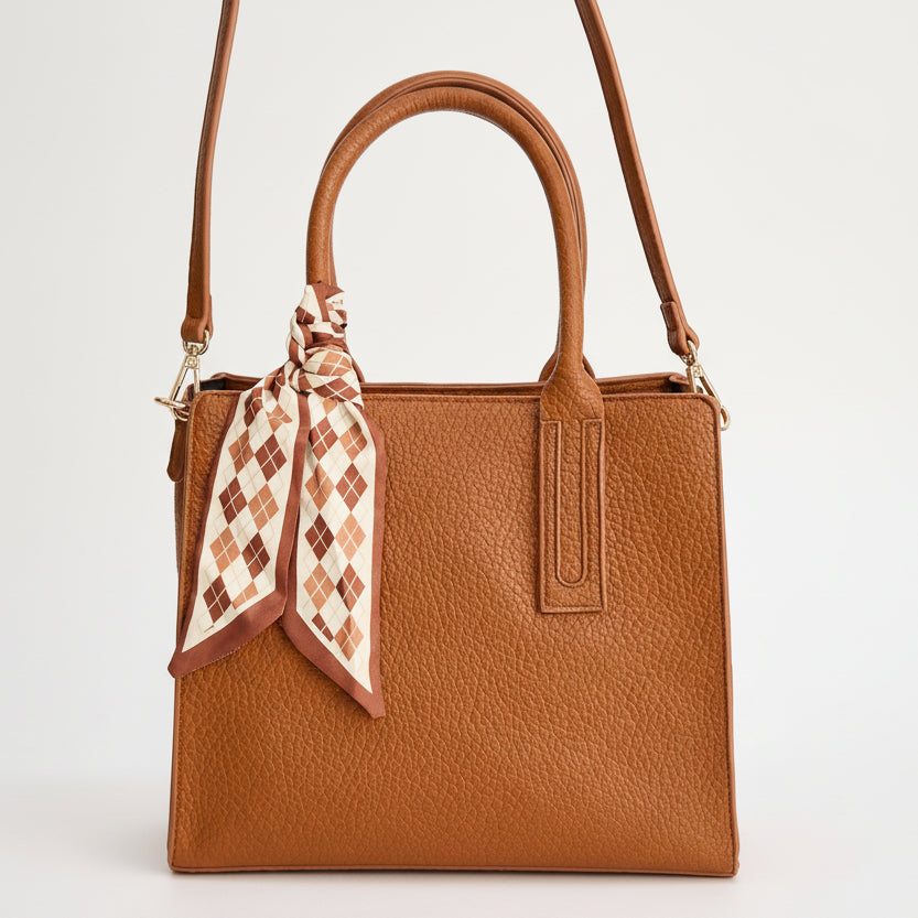 Brown handbag with a patterned scarf on a light gray background