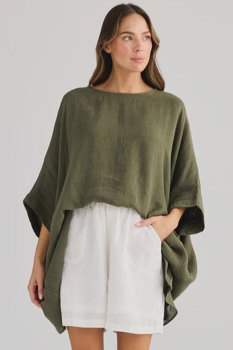 Woman wearing an olive green poncho over a white outfit on a gray background