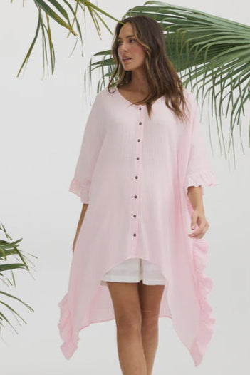 Woman wearing white shorts with a pink cover-up tunic against a white background with green palm leaves.