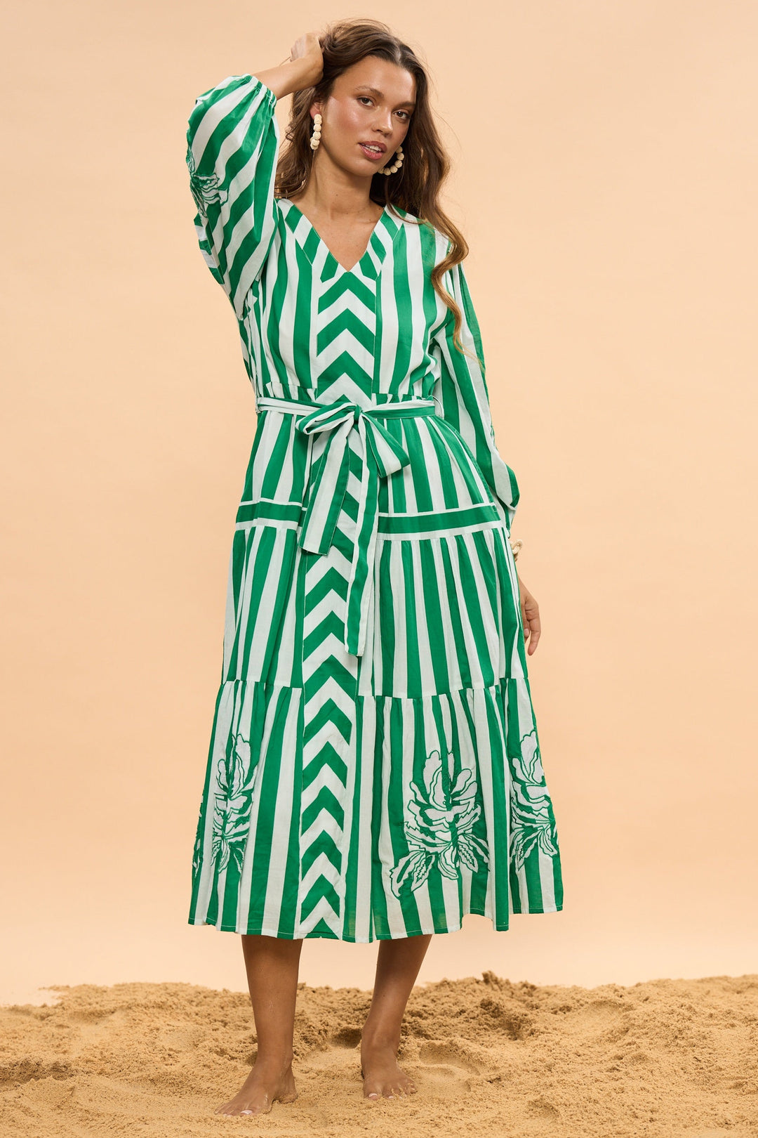Woman wearing a green and white striped dress standing on sand with a beige background