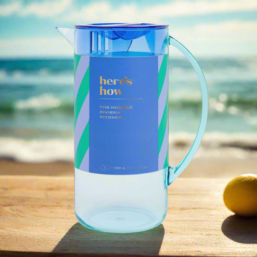 Clear plastic pitcher with blue lid and label on a light gray background