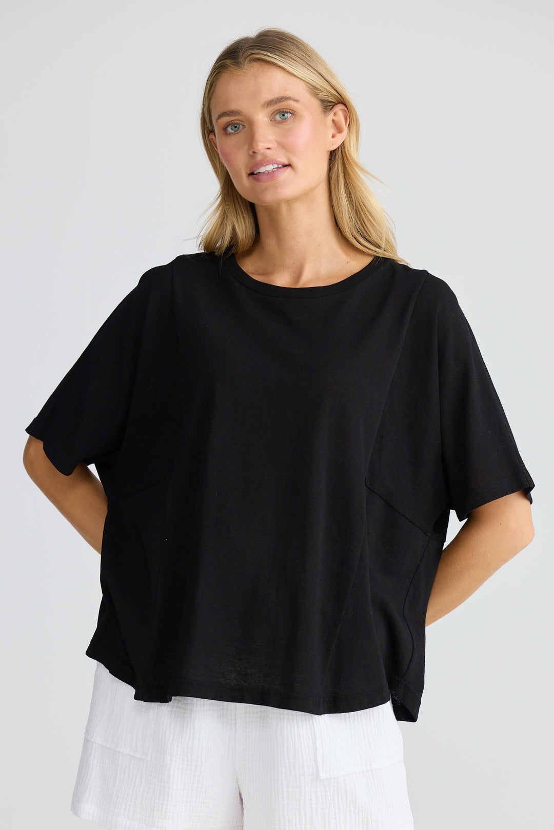 Woman wearing a black oversized top and white shorts on a plain background