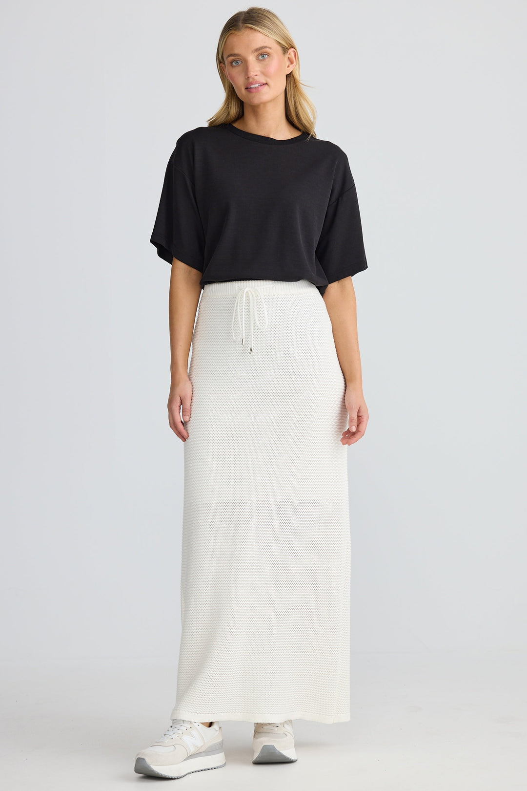 Woman wearing a black top and white skirt on a plain background