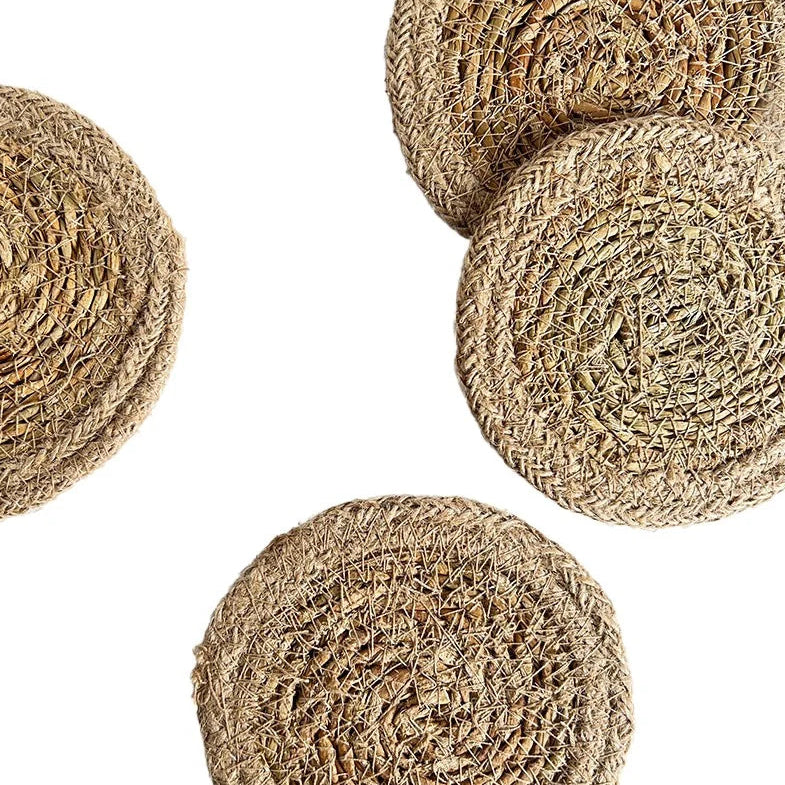 Four round woven seagrass or jute placemats in natural tan-brown tones, arranged on a plain white background.