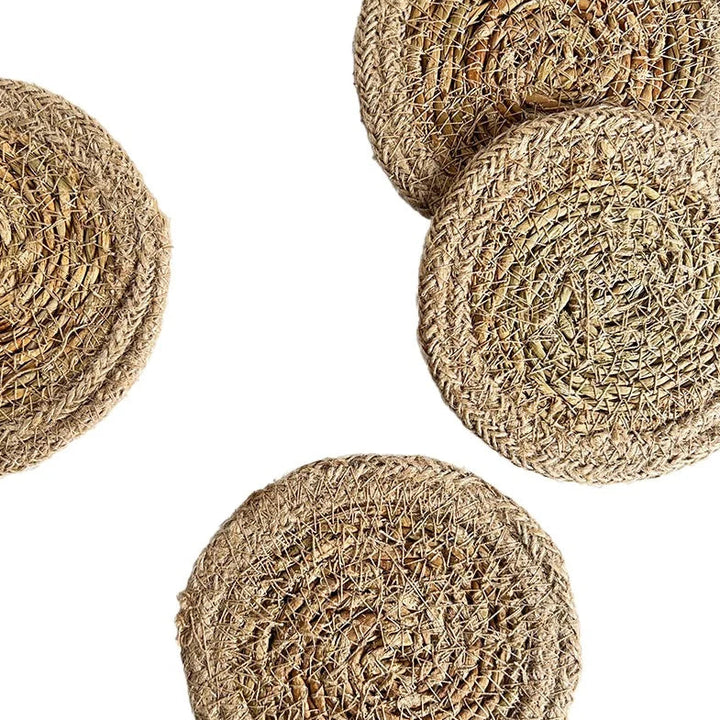 Four round woven seagrass or jute placemats in natural tan-brown tones, arranged on a plain white background.
