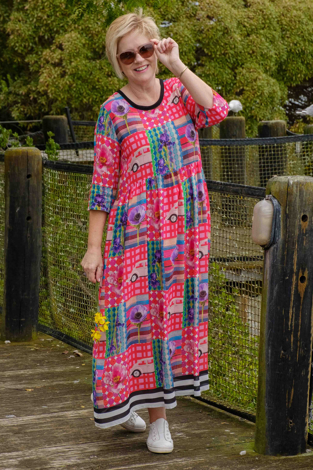 Woman in a colorful jellicoe dress standing on a wooden boardwalk with greenery in the background
