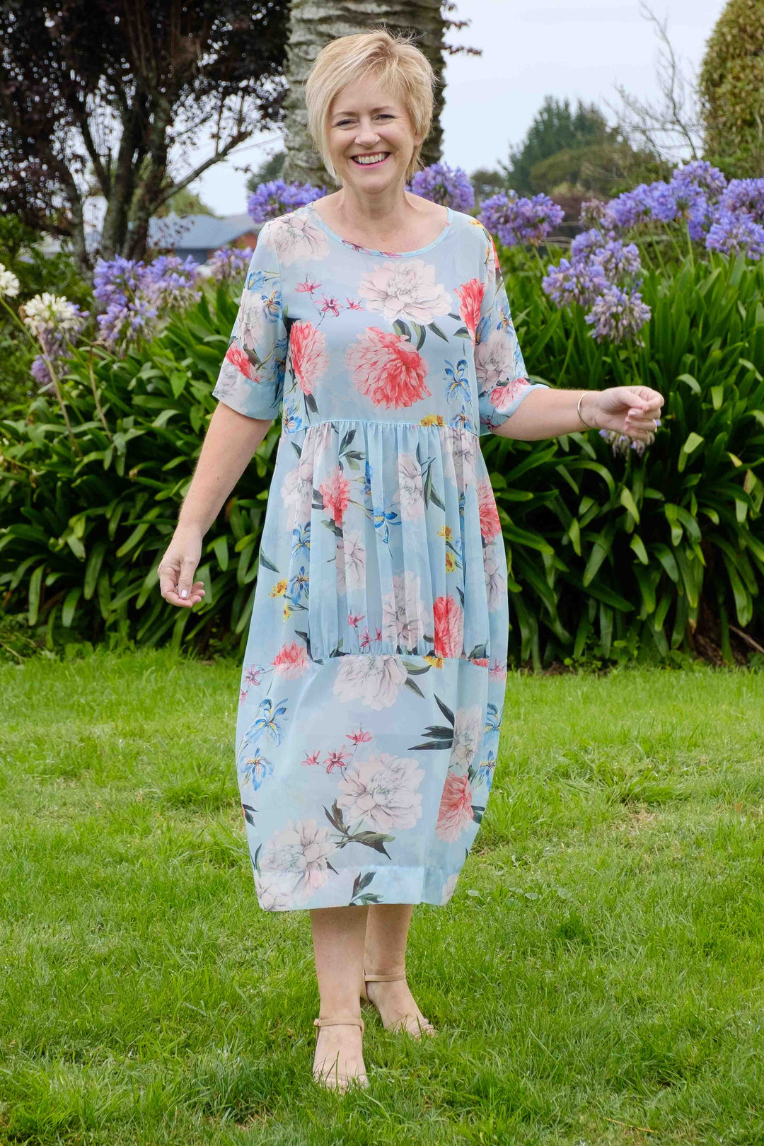Woman in a floral dress standing in a garden with greenery and flowers in the background
