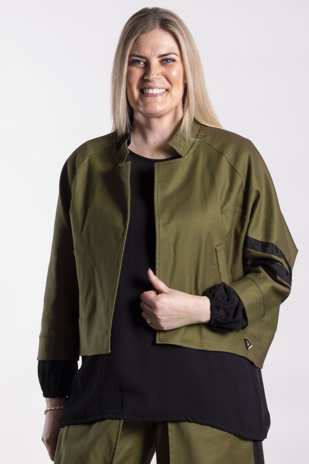 Woman wearing a long olive green coat with black accents on a white background