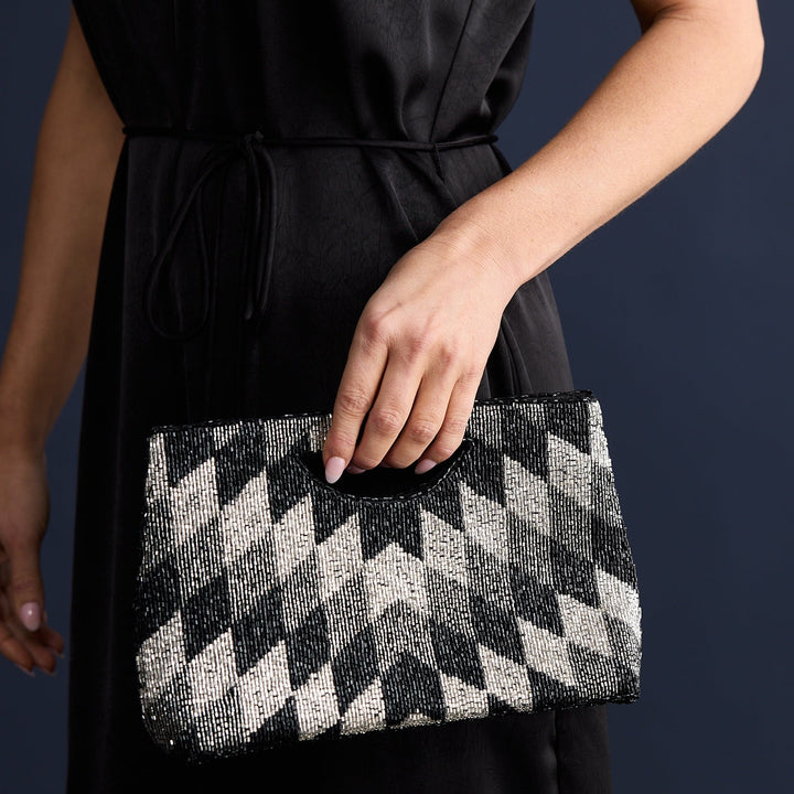 Person holding a black and white checkered clutch against a dark background