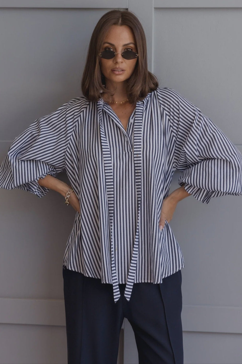 Woman wearing a striped shirt and sunglasses against a gray background