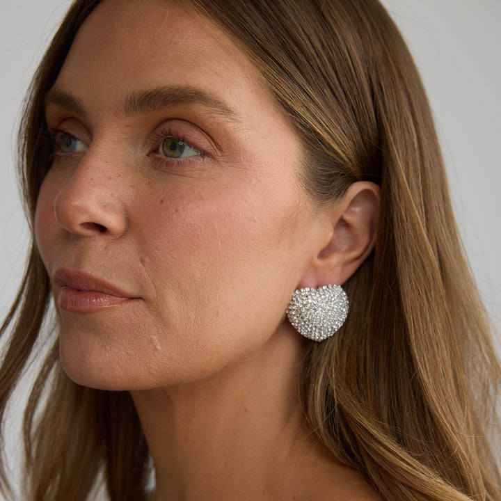 Close-up of a woman wearing a pair of heart-shaped earrings with a neutral background