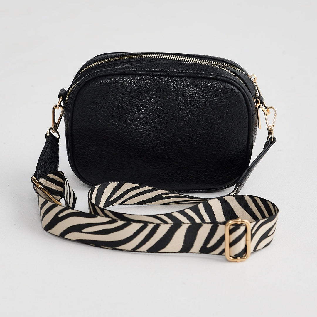 Black crossbody bag with zebra-striped strap on a light gray background