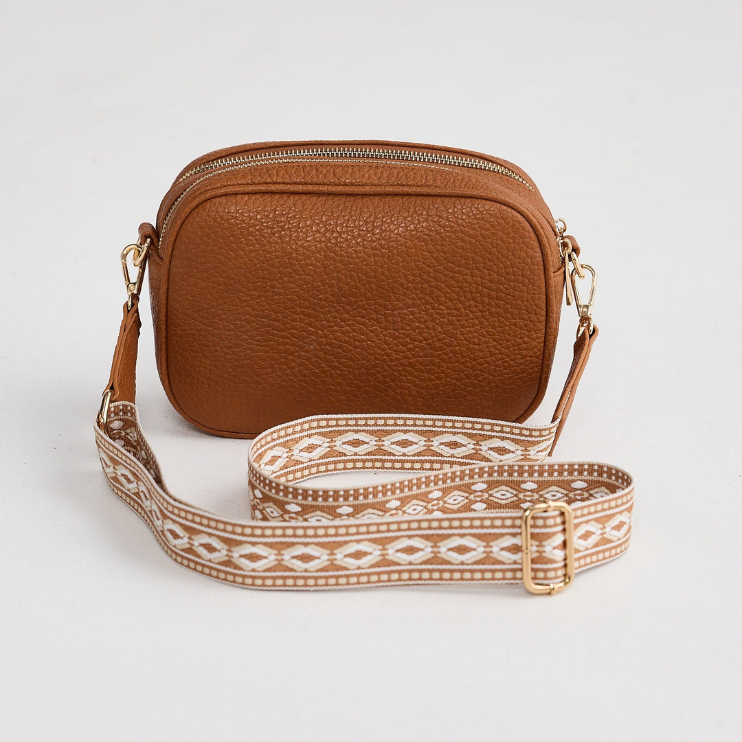 Brown leather crossbody bag with a patterned strap on a light gray background