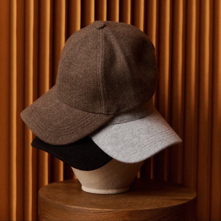 Three caps (brown, gray, black) on a wooden stand against an orange-brown paneled wall.