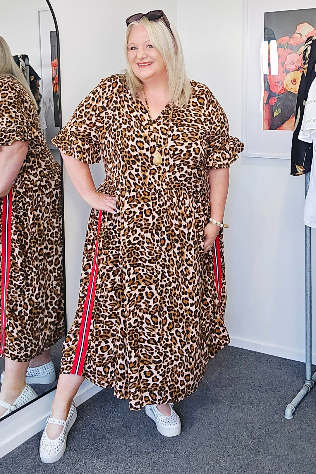 Woman wearing a leopard print dress in a room with a mirror and clothing rack.
