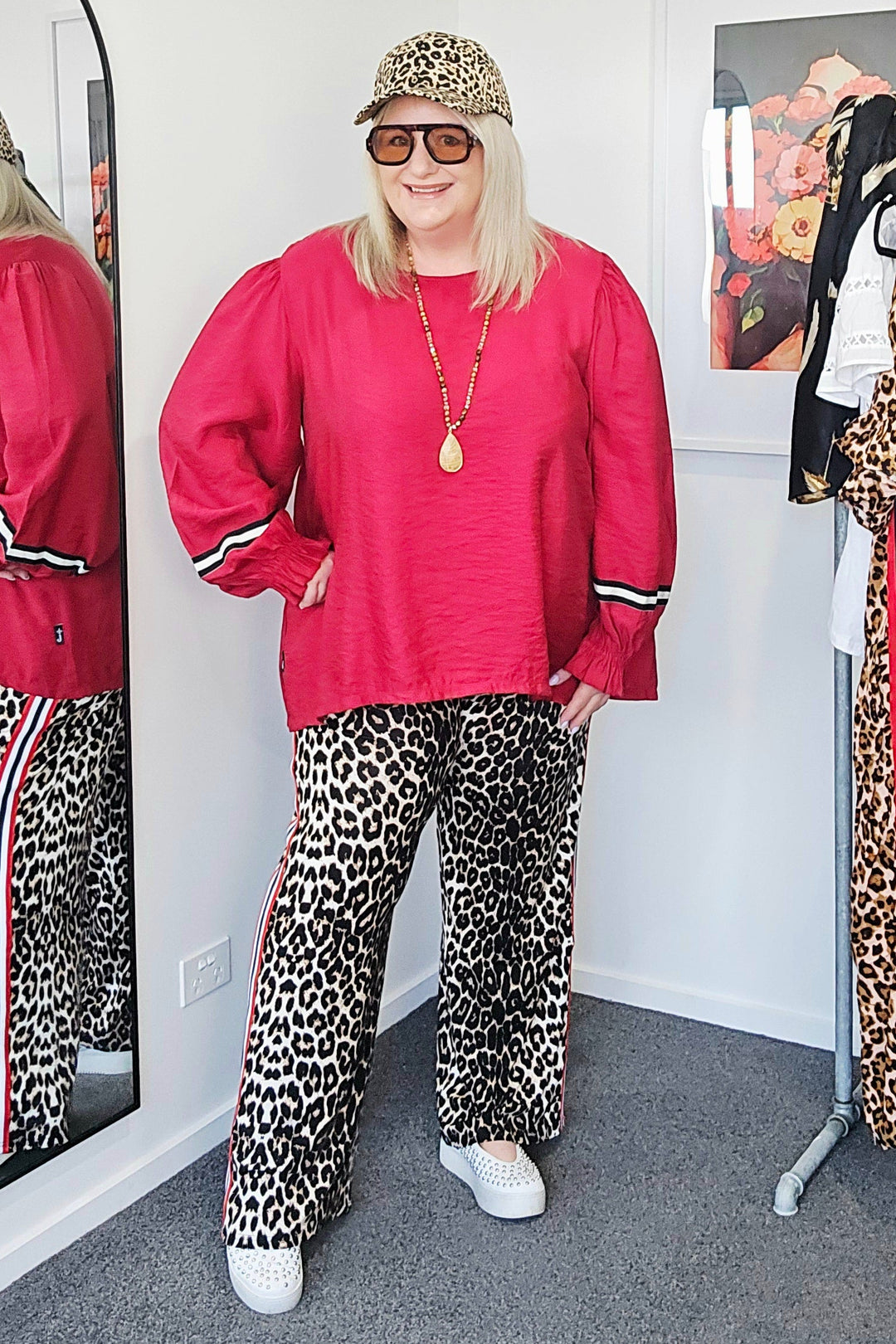 Person wearing a red sweatshirt and leopard print pants standing in front of a mirror.