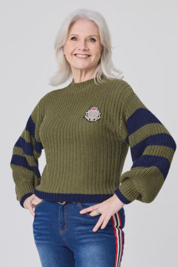 Woman wearing a green sweater with striped sleeves and blue jeans with red and white stripes on a white background