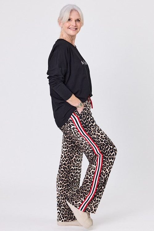 Woman wearing a black top and leopard print pants with red stripes on a white background