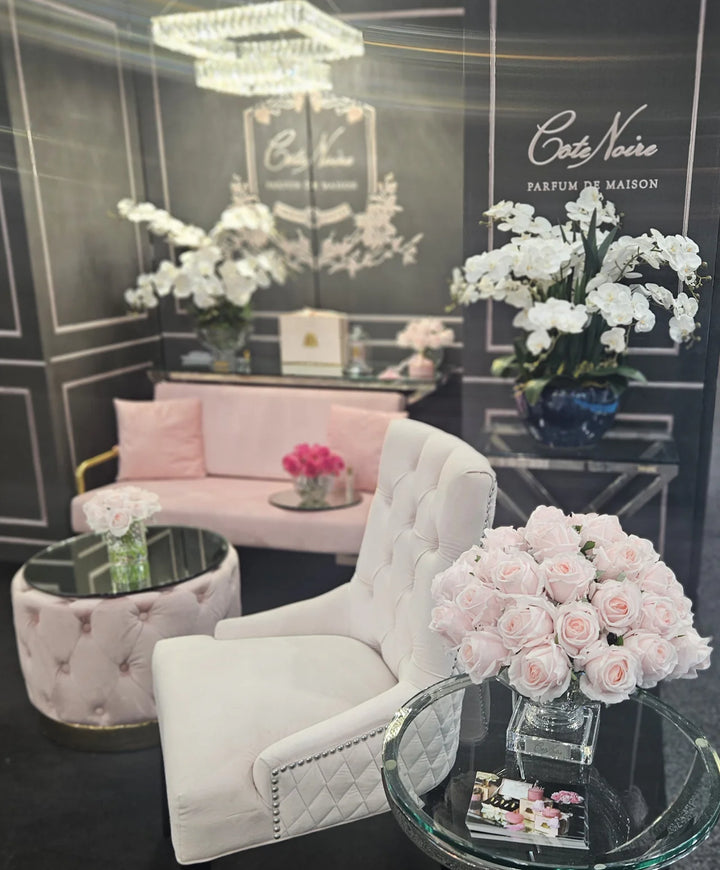 Luxurious interior with white armchair, pink sofa, and floral arrangements in a stylish room.