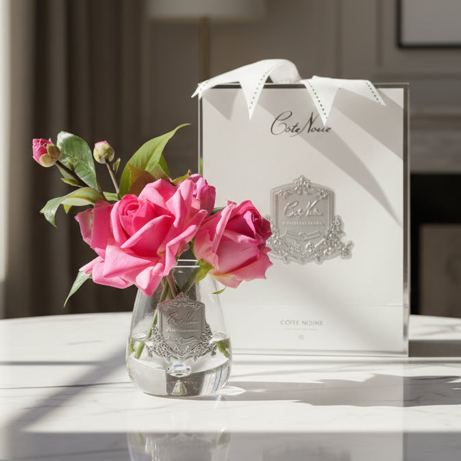 A handcrafted perfumed Tea Rose bouquet set in a clear gel, presented in a hand-blown clear tear drop vase with a silver signature Cote Noire badge. Accompanied by two small bottles of scented perfume, all enclosed in a Cote Noire ribboned box.