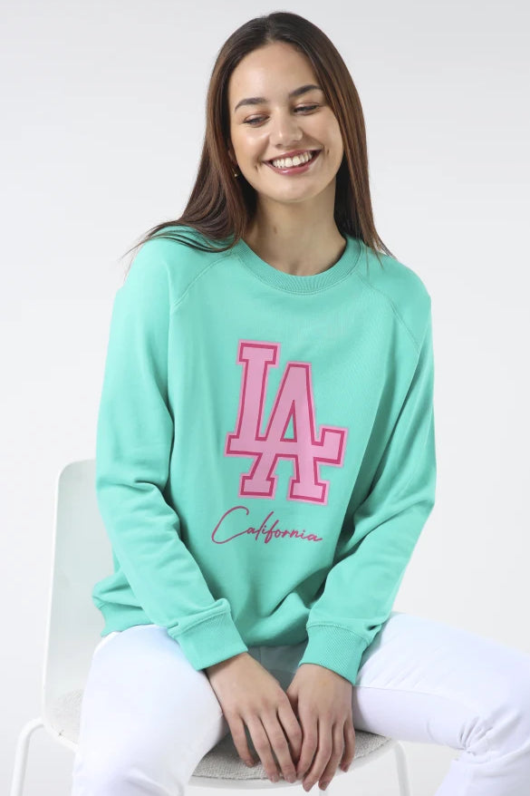 Woman wearing a teal sweatshirt with 'LA' and 'California' text on a white background
