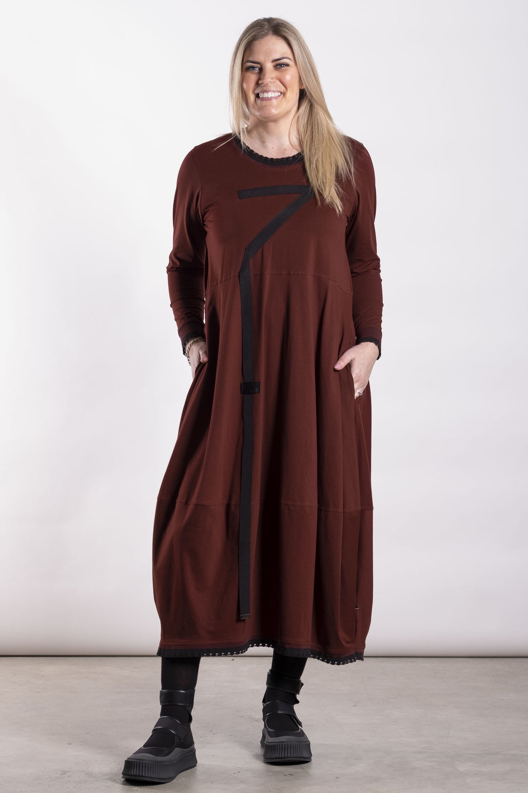 Woman wearing a long brown dress with black accents against a white background