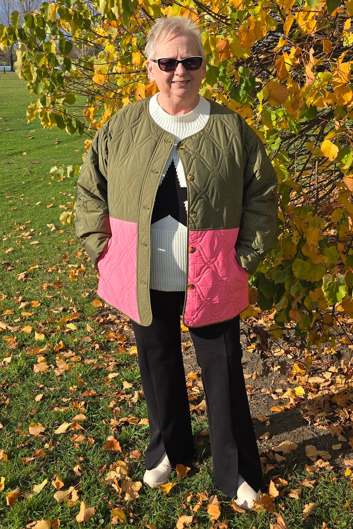 Lady wearing a green and pink quilted jacket standing in an autumn setting with yellow leaves.