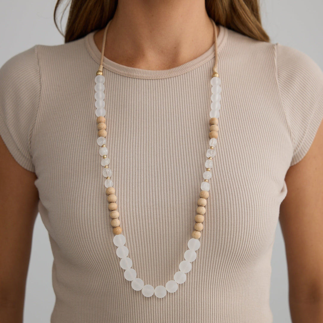 Person wearing a long necklace with white and beige beads on a plain background