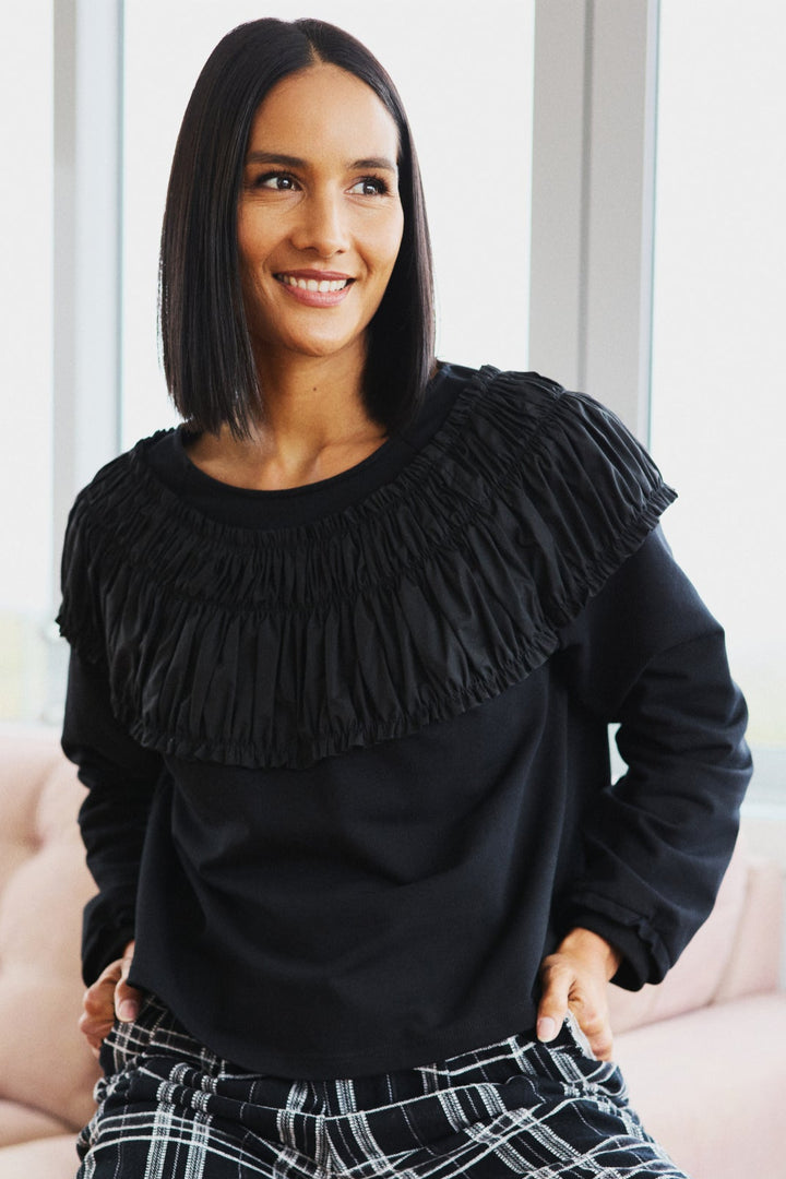 Woman wearing a black fringed sweater and plaid pants sitting on a pink couch.