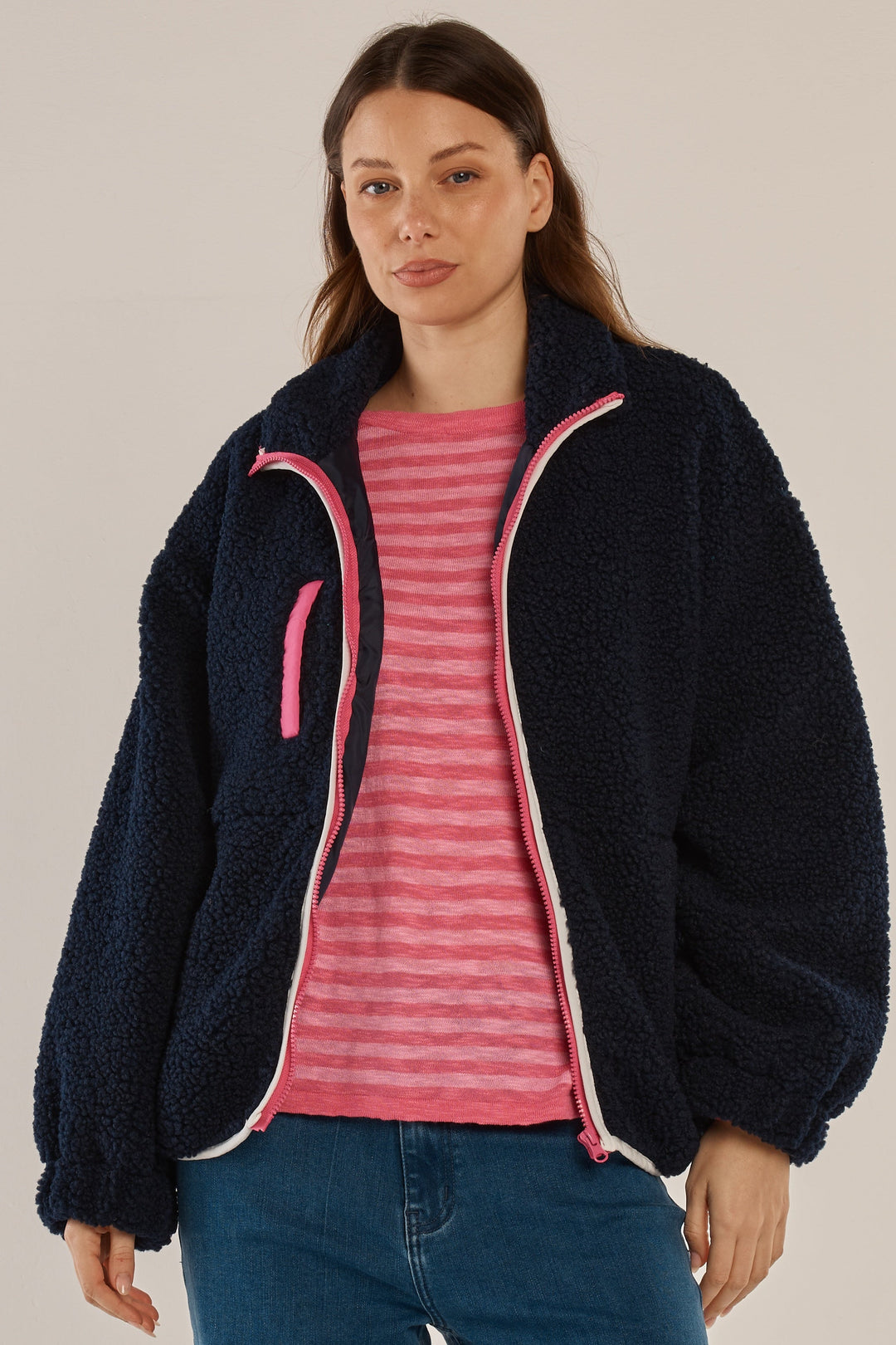 Woman wearing a navy fleece jacket with pink trim on a plain background