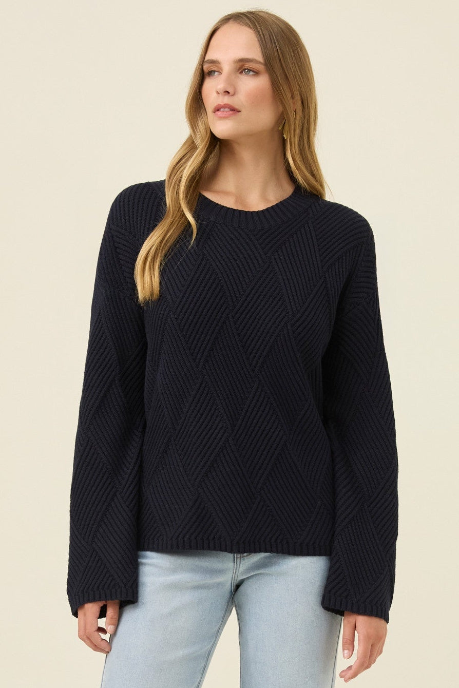 Woman wearing a black sweater and light blue jeans on a beige background