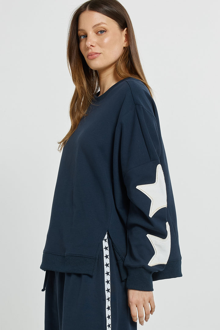 Woman wearing a navy blue sweatshirt with a white star design on a plain background