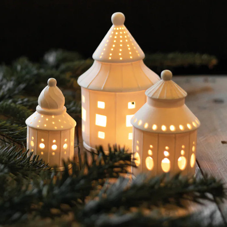 Three illuminated ceramic lanterns on a wooden surface with greenery