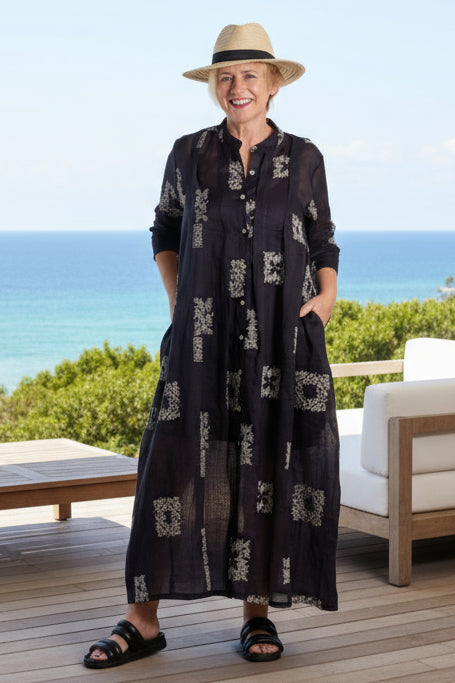 Woman wearing a long dark deeanne hobbs dress with patterns and a hat on.