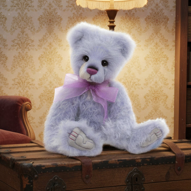 Charlie Bears plush collection plush toy named Natalia, with grey fur and a purple bow accessory, sitting on a wooden surface outdoors.