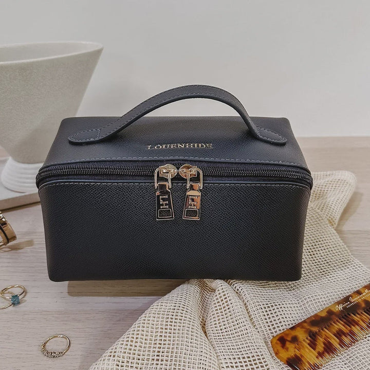 Navy Louenhide cosmetic case on a light wooden surface with a white bowl and accessories.