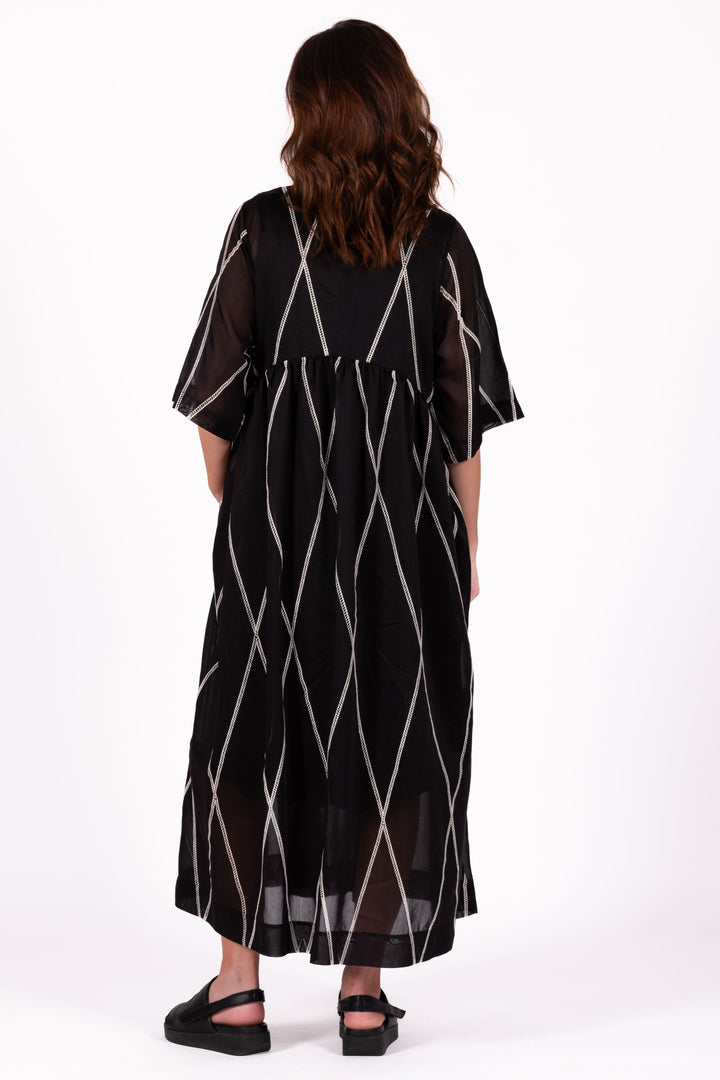Woman wearing a black dress with white geometric patterns on a white background